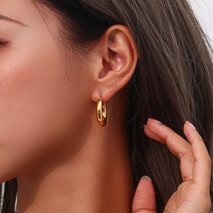 Dettaglio macro di orecchini a cerchio spessi placcati oro 18 carati su modella