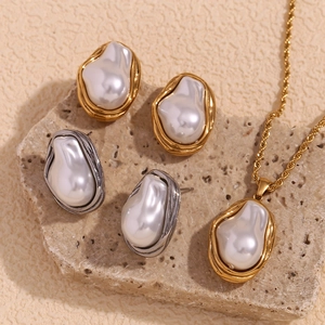 Detailed close-up of Baroque pearl earrings and rope chain necklace on textured stone