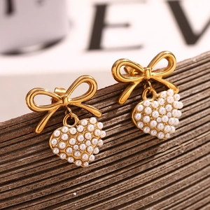 Close-up of golden bow earrings with pearl heart pendants on a textured display