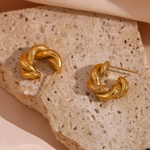 Detailed macro shot of gold twisted rope hoop earrings on beige stone and satin background