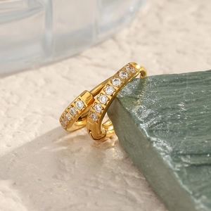 Vue macro de boucles d'oreilles dorées avec rangée de zircons posées sur une pierre verte