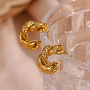 Macro shot of gold twisted hoop earrings hanging on a textured glass rim with soft fabric