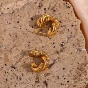 Close-up of golden twisted hoop earrings with textured finish on a natural stone base