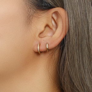 Gros plan de boucles d'oreilles huggies dorées avec zircons portées par un mannequin