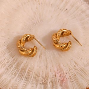 Macro detail of twisted gold C-shaped hoop earrings with textured spiral metal finish