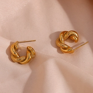 Macro detail of golden twisted C-shape hoop earrings on soft pink fabric background