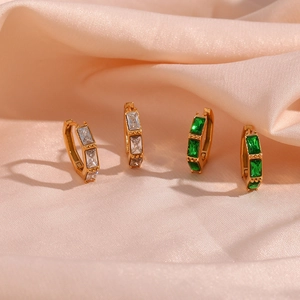 Close-up of gold bamboo style huggie earrings with green and clear zircon stones on silk