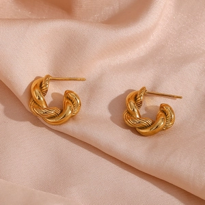 Detailed view of gold twisted metal hoop earrings resting on pink silk fabric background