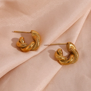 Detailed view of gold twisted hoop earrings with textured finish on pink satin background