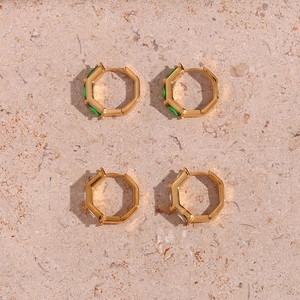 Detailed macro view of octagonal gold earrings with emerald green and white zircon stones