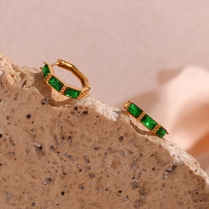 Detail of gold bamboo style earrings with green zircon stones on natural stone base