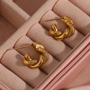 Macro detail of gold twisted C-shape hoop earrings on a soft pink velvet background
