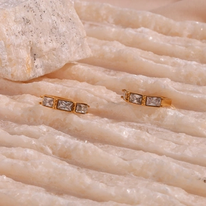 Detail shot of gold bamboo joint earrings with rectangular zircons on stone background