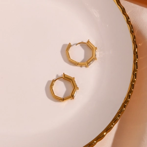 Detail of gold-plated hexagonal earrings with clear baguette zircons on a silk backdrop