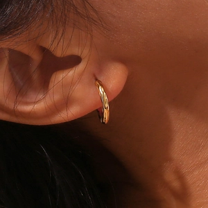 Macro view of gold lava hoop earring with irregular textured finish on model