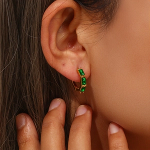 Close-up of gold huggie hoop earring with emerald cut green zircons on a model's ear