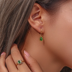Detalle de pendientes dorados y conjunto de anillo con gema verde en una modelo