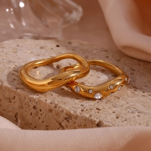 Detailed view of two 18K gold plated wavy rings with zirconia on a stone surface