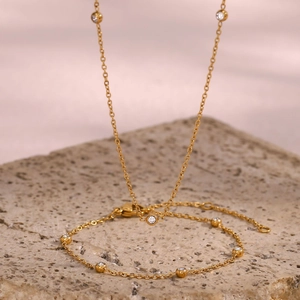 Elegante gouden ketting met ronde zirkonia-hangers op een getextureerde stenen achtergrond