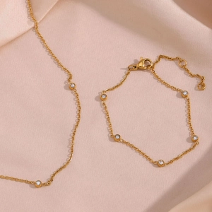 Detail van gouden kettingset met micro-kristallen op zachte roze satijnen stof
