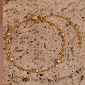 Detail van een goudkleurige kettingarmband met vijf zirkonia-stenen en een karabijnsluiting