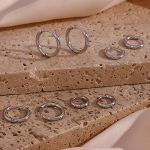 Polished silver stainless steel hoop earrings in various sizes on a beige travertine base