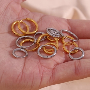 Polished stainless steel hoop earrings in gold and silver held in hand for scale
