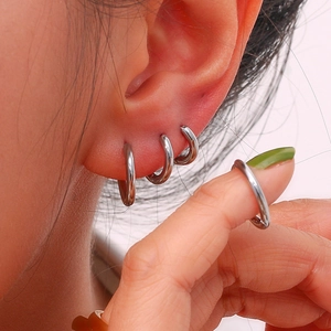 Macro view of stacked silver polished stainless steel hoop earrings on ear