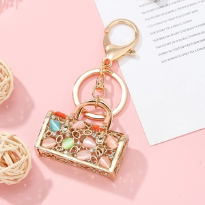Porte-clés sac à main doré avec strass colorés et opales sur fond rose élégant