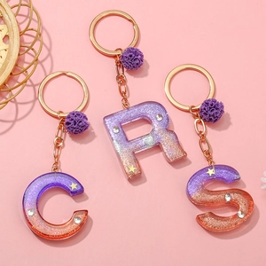 Detail of alphabet resin keychains with purple gradient, star glitter, and gold ring