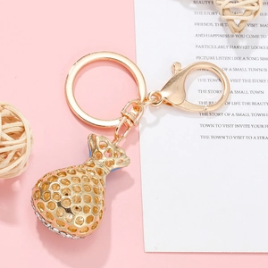 Golden money bag keychain with hollow design and white rhinestones on pink background