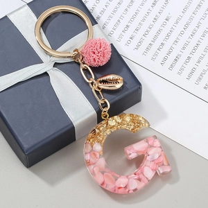 Dettaglio macro del portachiavi a lettera G in resina con scaglie rosa e foglie d'oro