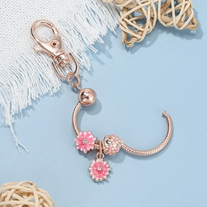 Rose gold daisy keychain with pink enamel charms and snake chain on a light blue background