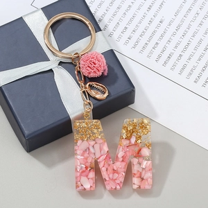 Dettaglio portachiavi lettera M in resina rosa con scaglie dorate e pompon in peluche