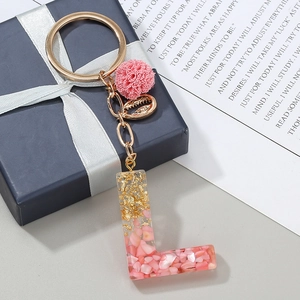 Dettaglio portachiavi lettera L in resina con pietre rosa, foglia d'oro e un pompon