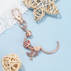 Rose gold DIY keychain with sunflower and winged key charms on a light blue background