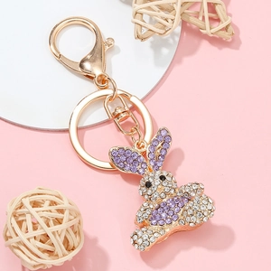 Golden bunny keychain with purple rhinestones on a decorative pink background