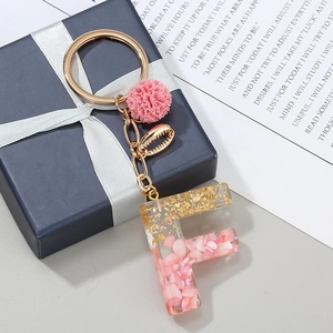 Dettaglio portachiavi lettera F in resina rosa con foglie d'oro, pompon e ciondolo a conchiglia