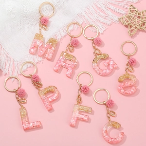 Portachiavi con lettere in resina sfumata rosa, glitter oro, pompon e ciondolo a conchiglia