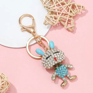 Détails d'un porte-clés lapin bleu doré orné de cristaux brillants sur fond rose doux