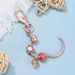 Rose gold DIY mushroom keychain with floral charm and red enamel bead on blue surface