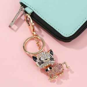 Détail macro du porte-clés chat doré orné de strass roses et blancs sur un portefeuille