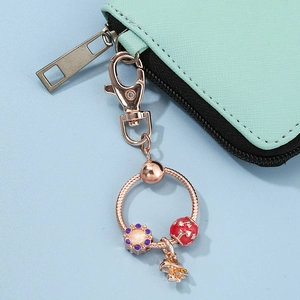 Rose gold keychain with purple floral bead and mushroom charm on a mint leather wallet