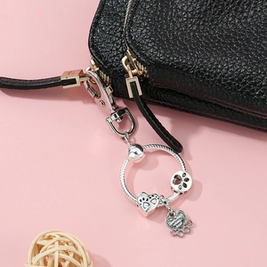 Silver metal animal paw and heart bead charm keychain on a black leather handbag