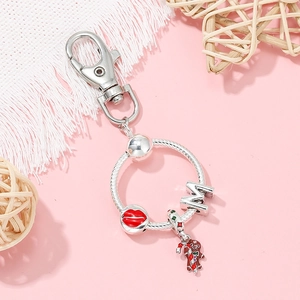 Silver keychain with gingerbread man, red lips, and M letter charms on pink background