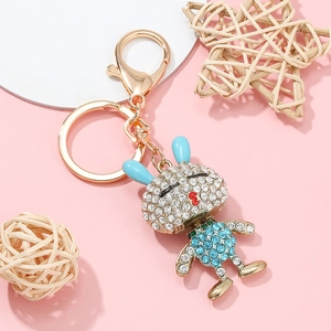 Porte-clés lapin doré orné de strass bleus sur fond rose avec décor tressé