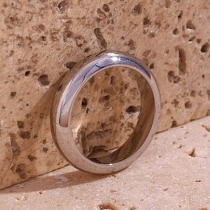 Macro shot of silver minimalist polished stainless steel band ring on beige stone