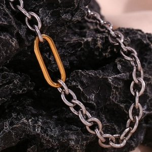 Detail of silver chain link necklace with a gold oval connector on black stone