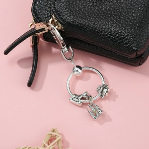 Silver charm keychain with rocking horse and castle pendant on black leather handbag