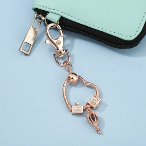 Rose gold heart keychain with travel camera and hot air balloon charms on green pouch